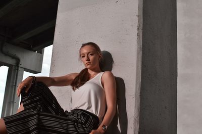 Portrait of young woman looking away while standing against wall