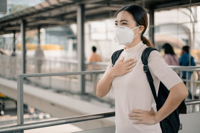 Woman looking away wearing pollution mask while standing on footbridge