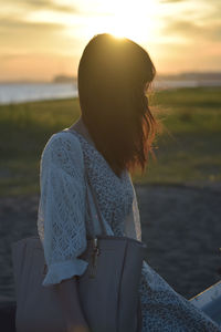 Rear view of woman with umbrella against sky during sunset