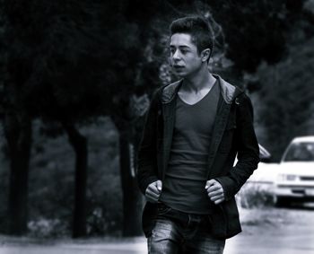 Young man looking away against trees