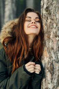 Portrait of smiling young woman against tree trunk