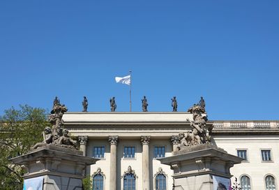 Low angle view of statue against building against clear blue sky