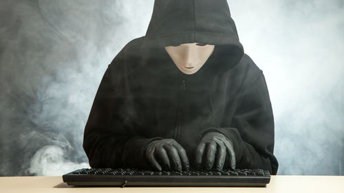 Woman wearing mask while typing on keyboard against blurred background