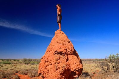 Shirtless man standing on rock at field against sky