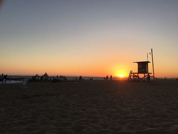 Silhouette people on beach against clear sky during sunset