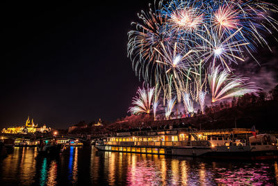 Low angle view of illuminated firework display over river against sky at night