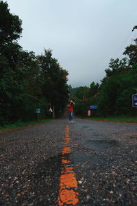 Surface level of man walking on road against sky