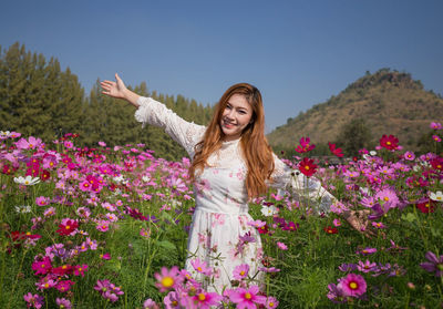 Smiling young woman standing by flowering plants on field