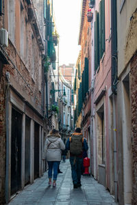 Rear view of people walking amidst buildings at alley in city