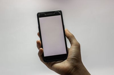 Close-up of hand holding mobile phone against white wall