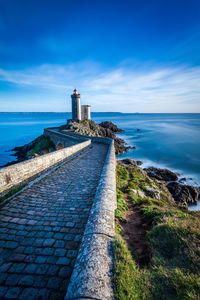 Lighthouse by sea against blue sky