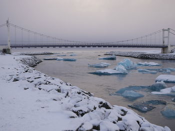 Suspension bridge over lake against sky during winter