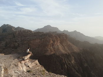 High angle view of young man sitting on rock against sky