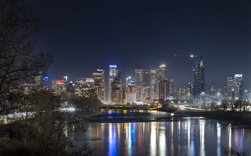 Illuminated buildings by river against sky at night