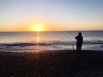 Silhouette man standing on beach against clear sky during sunset