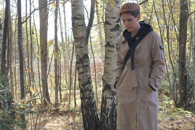 Young man standing by tree trunk in forest