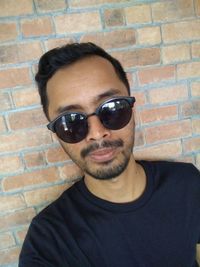 Portrait of young man wearing sunglasses against brick wall