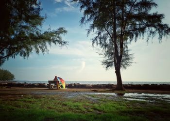 Woman with umbrella sitting at beach against sky