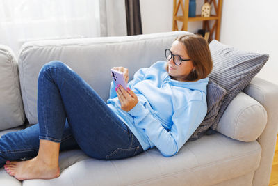 Young woman using digital tablet while sitting on sofa at home