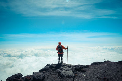 Rear view of man standing on cliff against cloudy sky