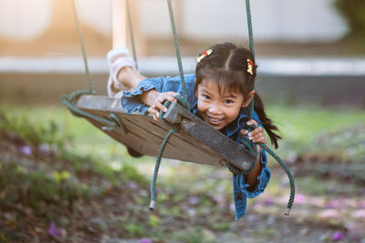 Portrait of happy girl lying on swing at playground
