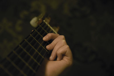 Cropped hand playing guitar against wall