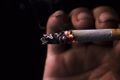 Cropped image of hand holding cigarette over black background