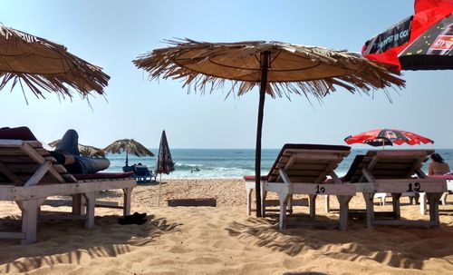 Lounge chairs and parasols on beach against clear sky