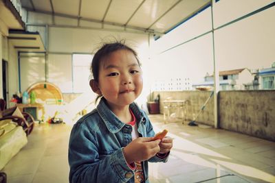 Portrait of smiling girl eating fruit while standing at home