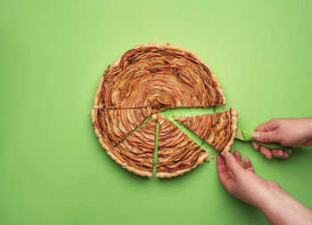 Cropped hand holding apple pie on green background