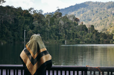 Rear view of woman standing by railing against lake