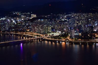 Illuminated bridge over river by buildings in city at night