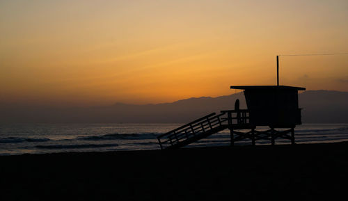 Silhouette lifeguard hut at beach against sky at dusk