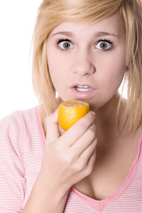Portrait of shocked young woman holding lemon against white background