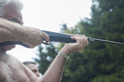 Close-up of senior man holding gun against clear sky
