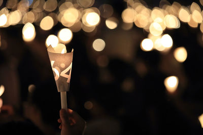 Close-up of hand holding illuminated candles against blurred background