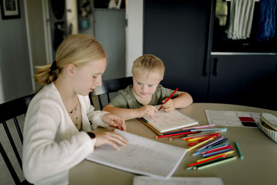 Girl doing homework by brother with down syndrome drawing in book at home