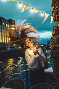 Young woman with tousled hair holding illuminated string light at night