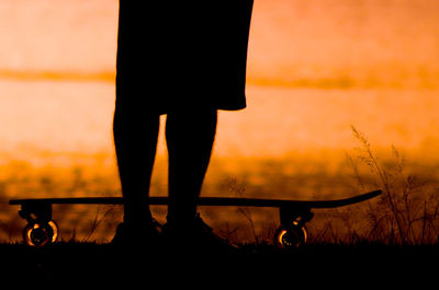 Low section of silhouette man standing against orange sky