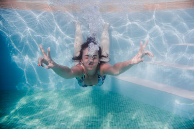 Woman gesturing while swimming underwater in pool