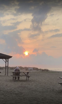 Rear view of men on beach against sky during sunset