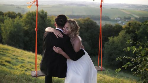 Couple embracing on rope swing at mountain