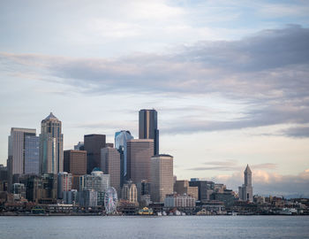 View of city at waterfront against cloudy sky