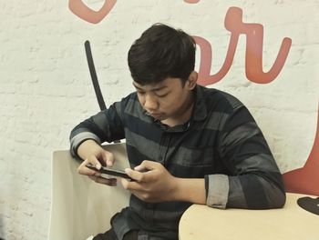 Young man using mobile phone while sitting on wall