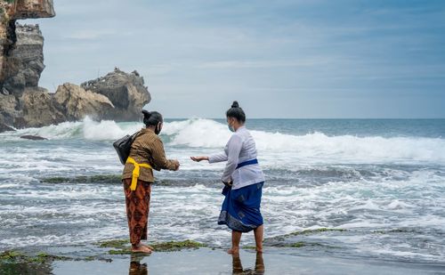 Rear view of men standing at beach against sky