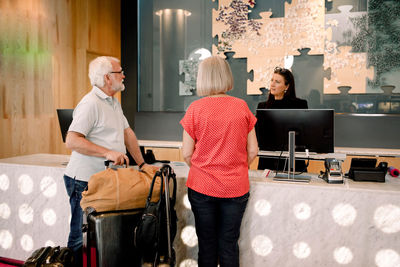 Senior couple talking to receptionist while standing at reception in hotel