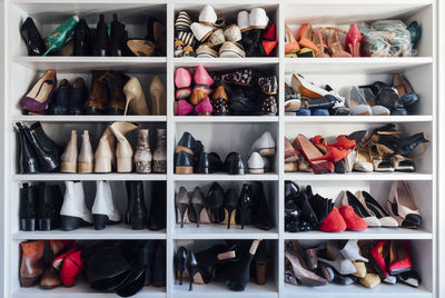 Modern white closet and square shelves with female colorful expensive high heels shoes and sneakers