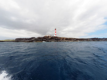 Lighthouse and buildings by sea against sky