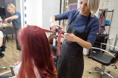 Hairdresser curls using curling irons to long hair girl front of the mirror in the salon hairdresser