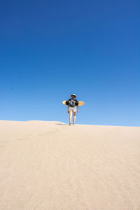 Full length rear view of woman walking with sandboard in desert